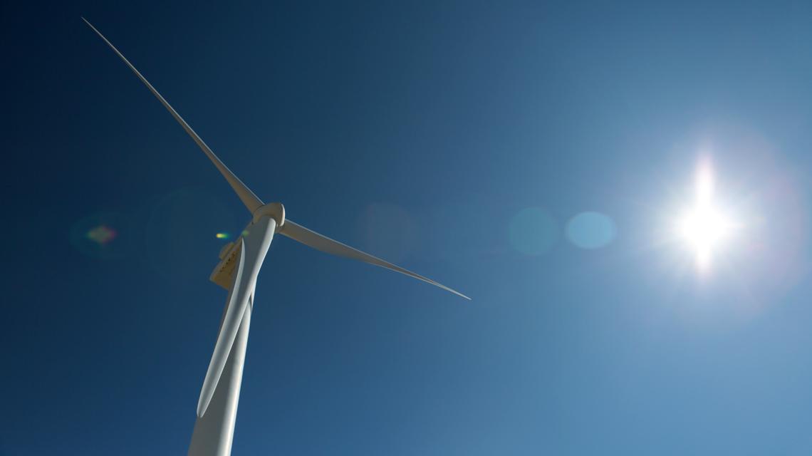 A single white wind turbine against bright blue sky